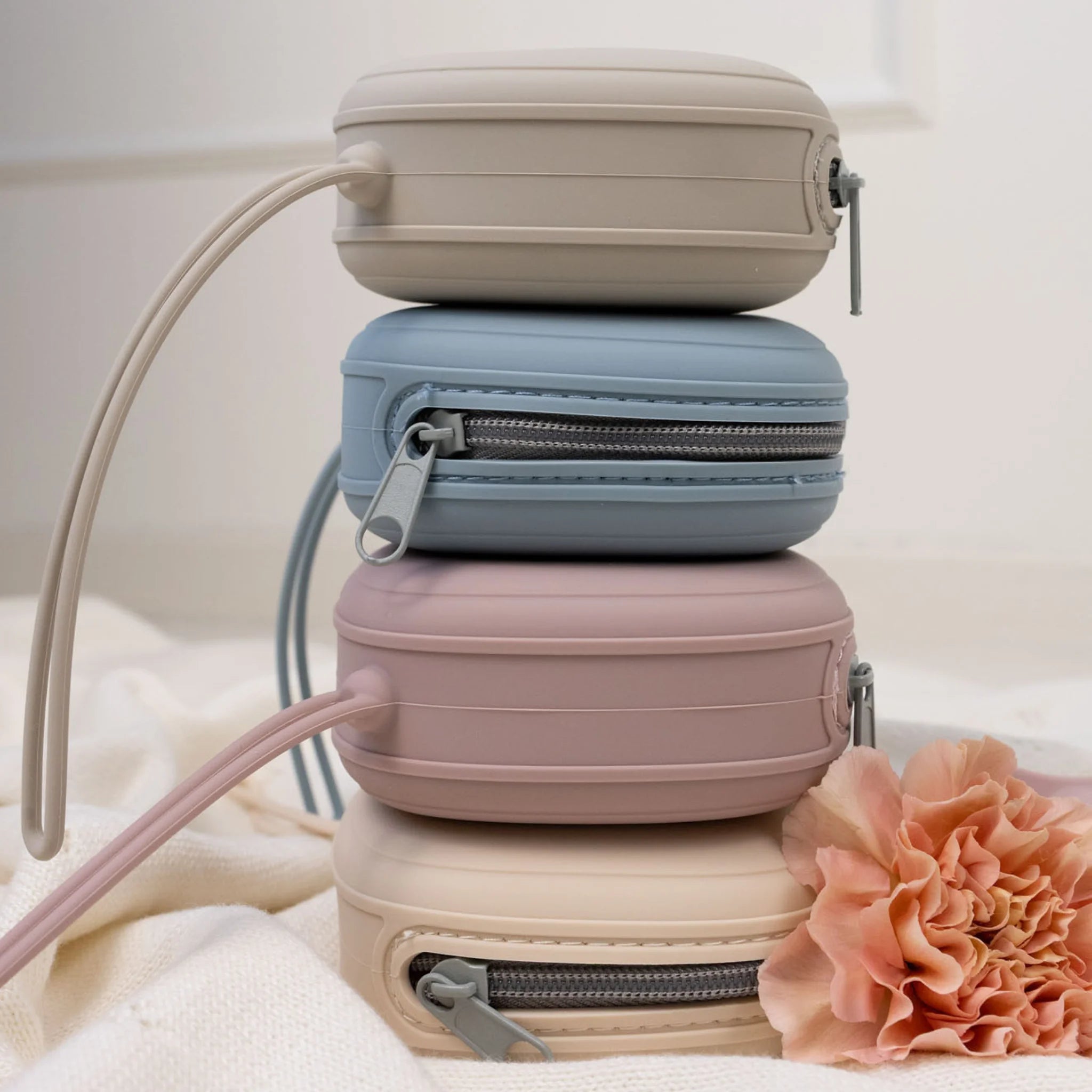 Siliconen fopspeenhouders van Mom Glowth in vier kleuren kiezelbeige, etherblauw, lila en nude beige gestapeld – BPA-vrij, food-grade siliconen, compact met rits