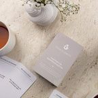 Postpartum gesprekskaarten van Mom Glowth uitgespreid naast bewaarbox, kopje thee en bloemen – cadeau voor nieuwe mama's in het vierde trimester