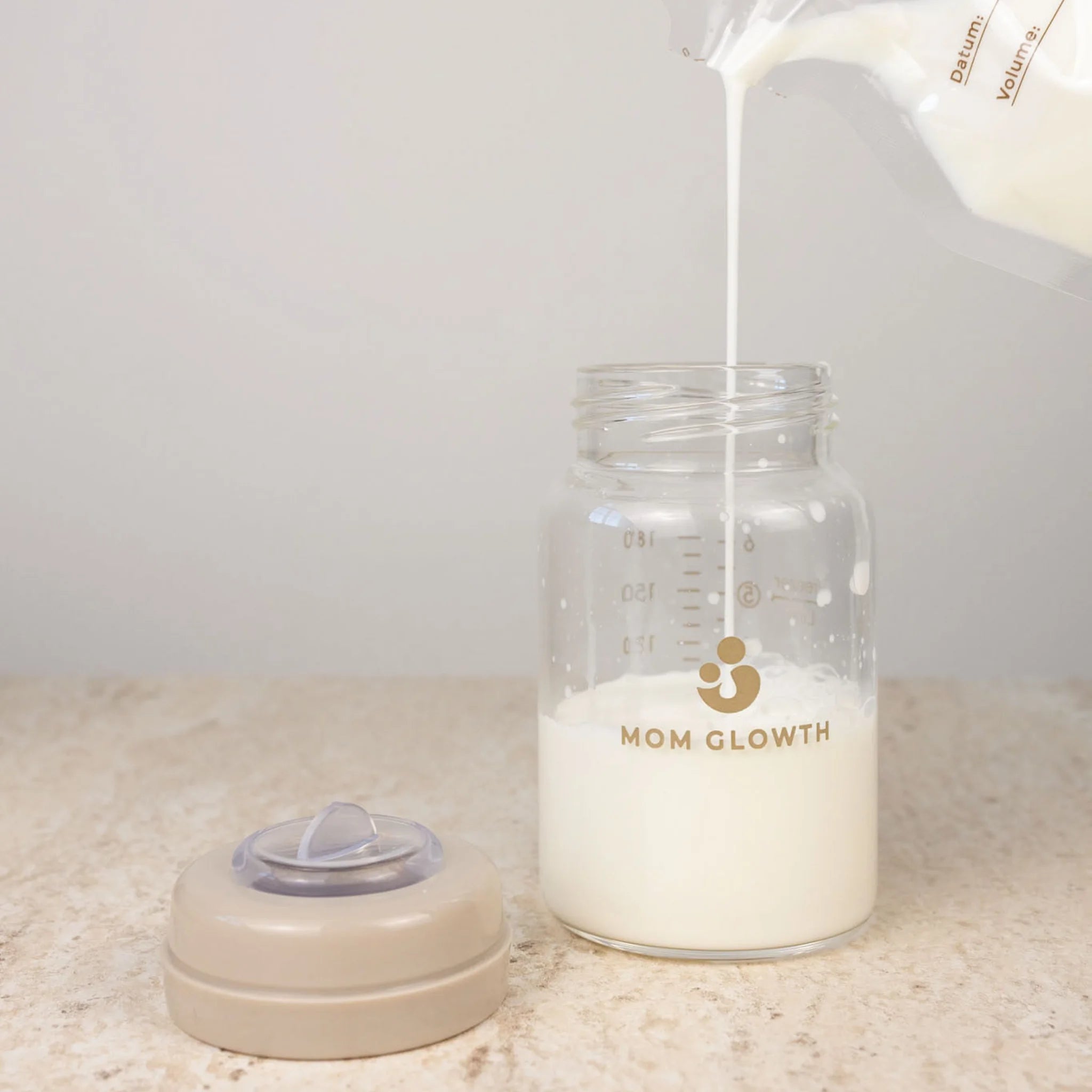 Moedermelk wordt ingeschonken in glazen bewaarflesje van Mom Glowth met maatstreepjes – lekvrije schroefdop, borosilicaatglas, BPA-vrij